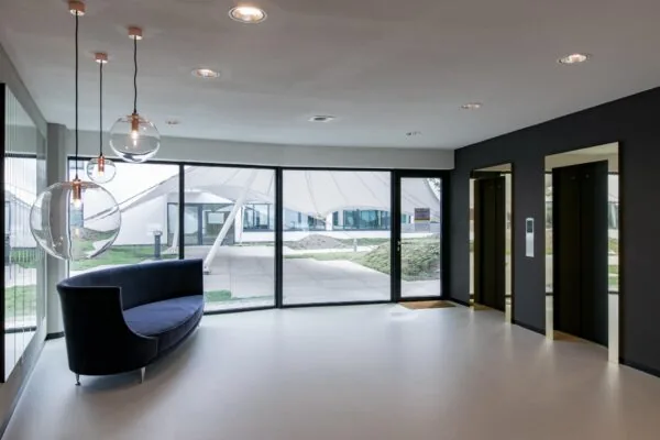 Moderne lobby van een kantoorgebouw aan de Grote Marktstraat met glazen hanglampen, een donkerblauwe bank en twee liften.